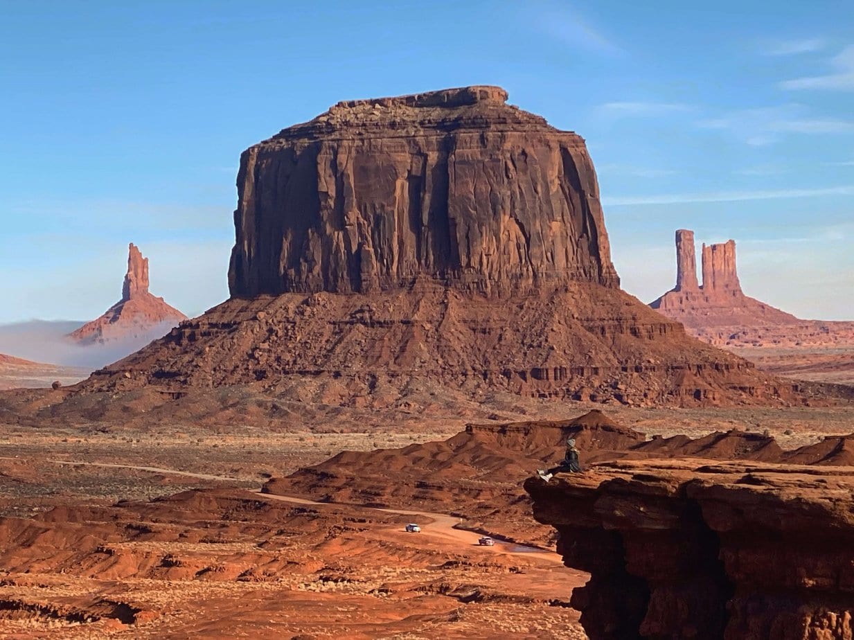 Girl in a Black Coat Siting on a Rock In Front of Large Butte