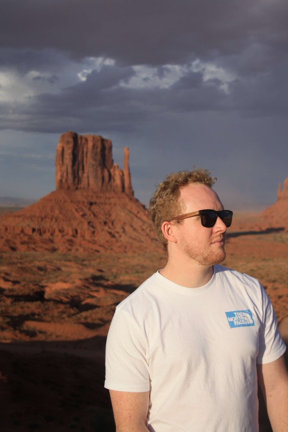 Man with a White Shirt and Black Glasses Looking to the Left in Front of a Rock Structure