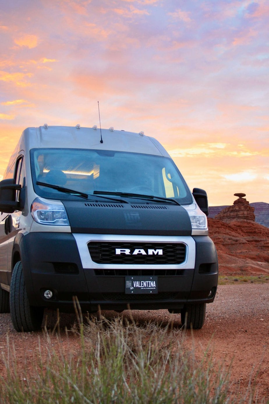 Ram Van Parked Behind a Bush in the Desert with a Pink and Yellow Sky in the Background