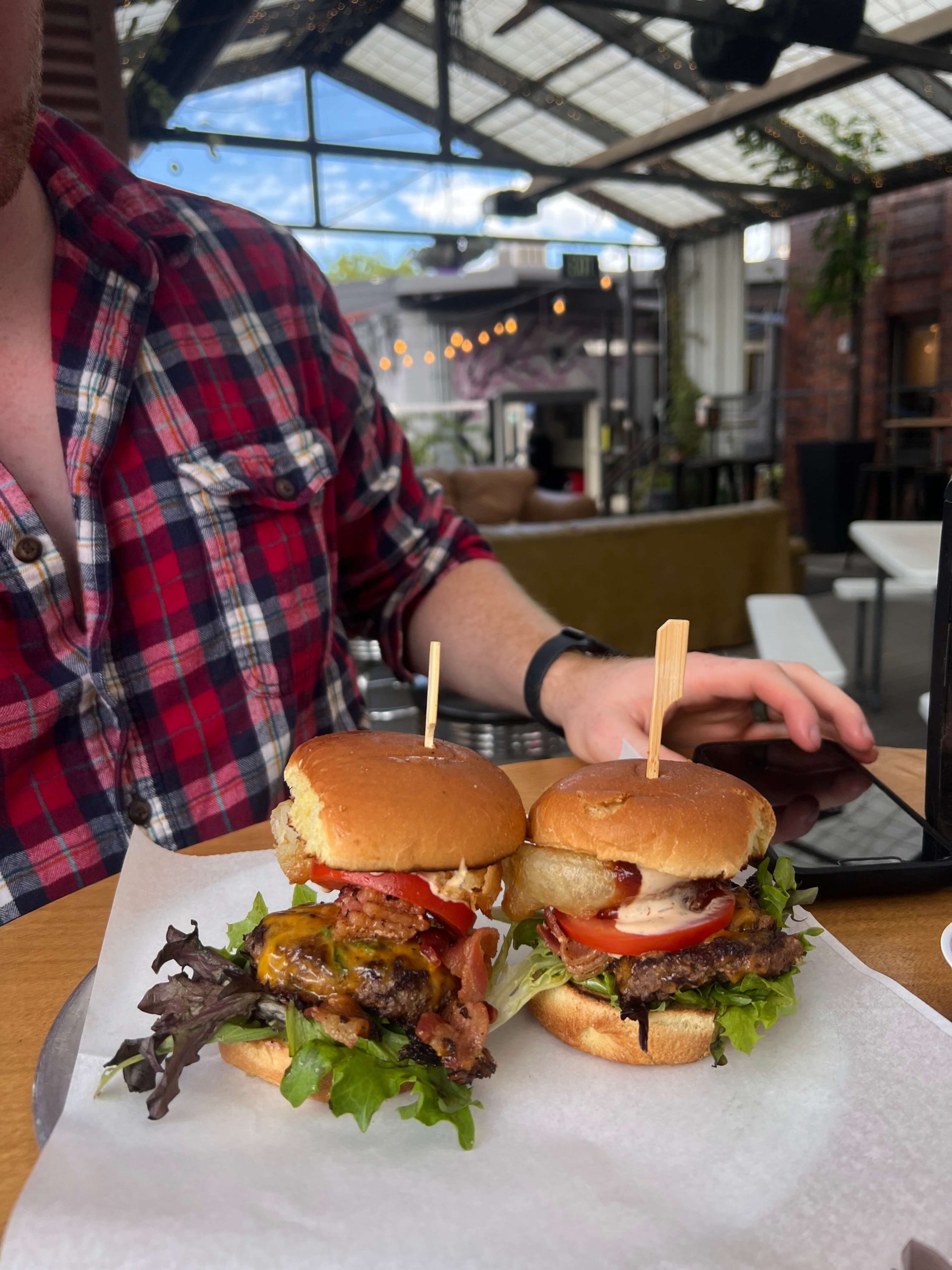 A Man with a Red Plaid Shirt about to Eat Two Cheeseburgers with Bacon and Lettuce