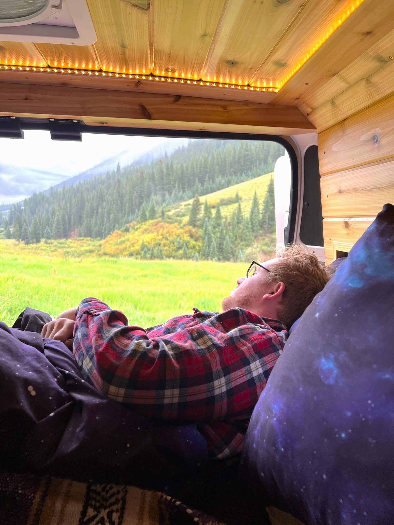 Man in Red Plaid Sleeping in Purple Bedding overlooking Nature