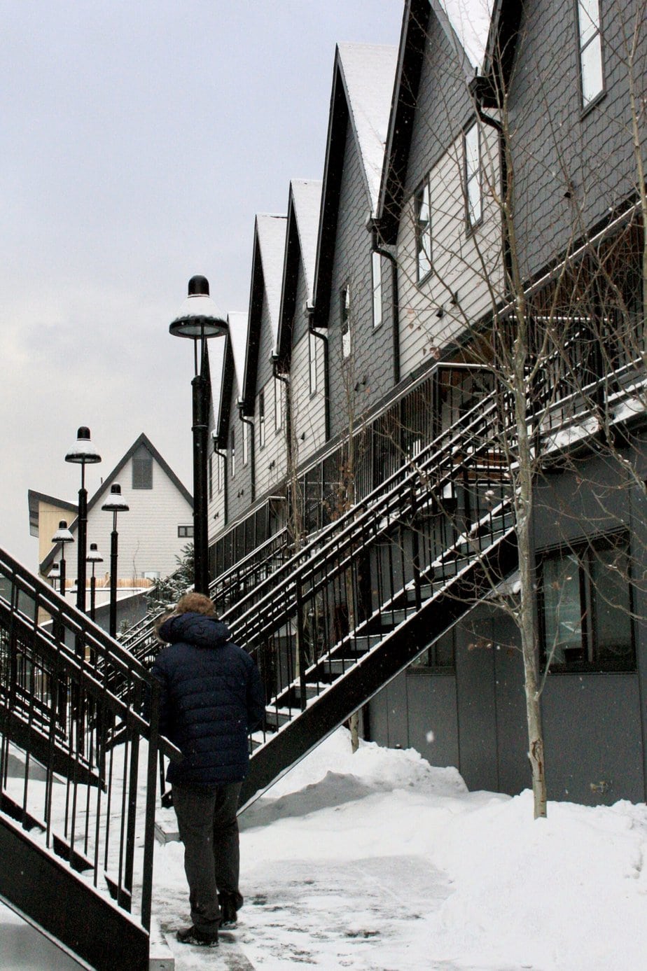 Man in Blue Coat Walking in Snow at Hotel with Pointy Buildings