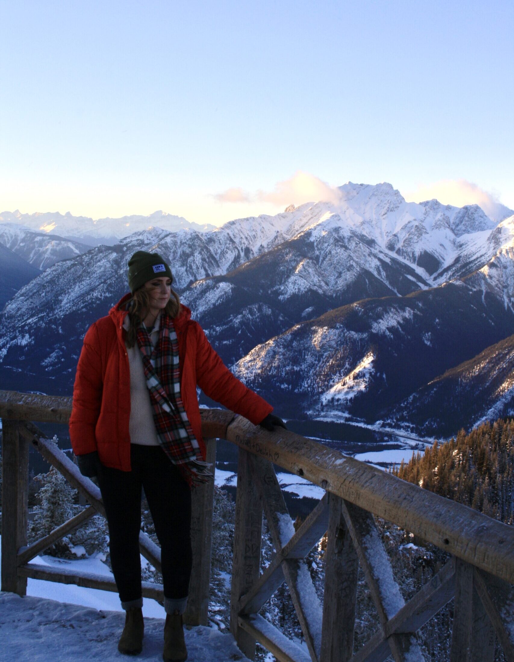 Girl in a Red Coat Holding onto a Wood Rail on top of a mountain