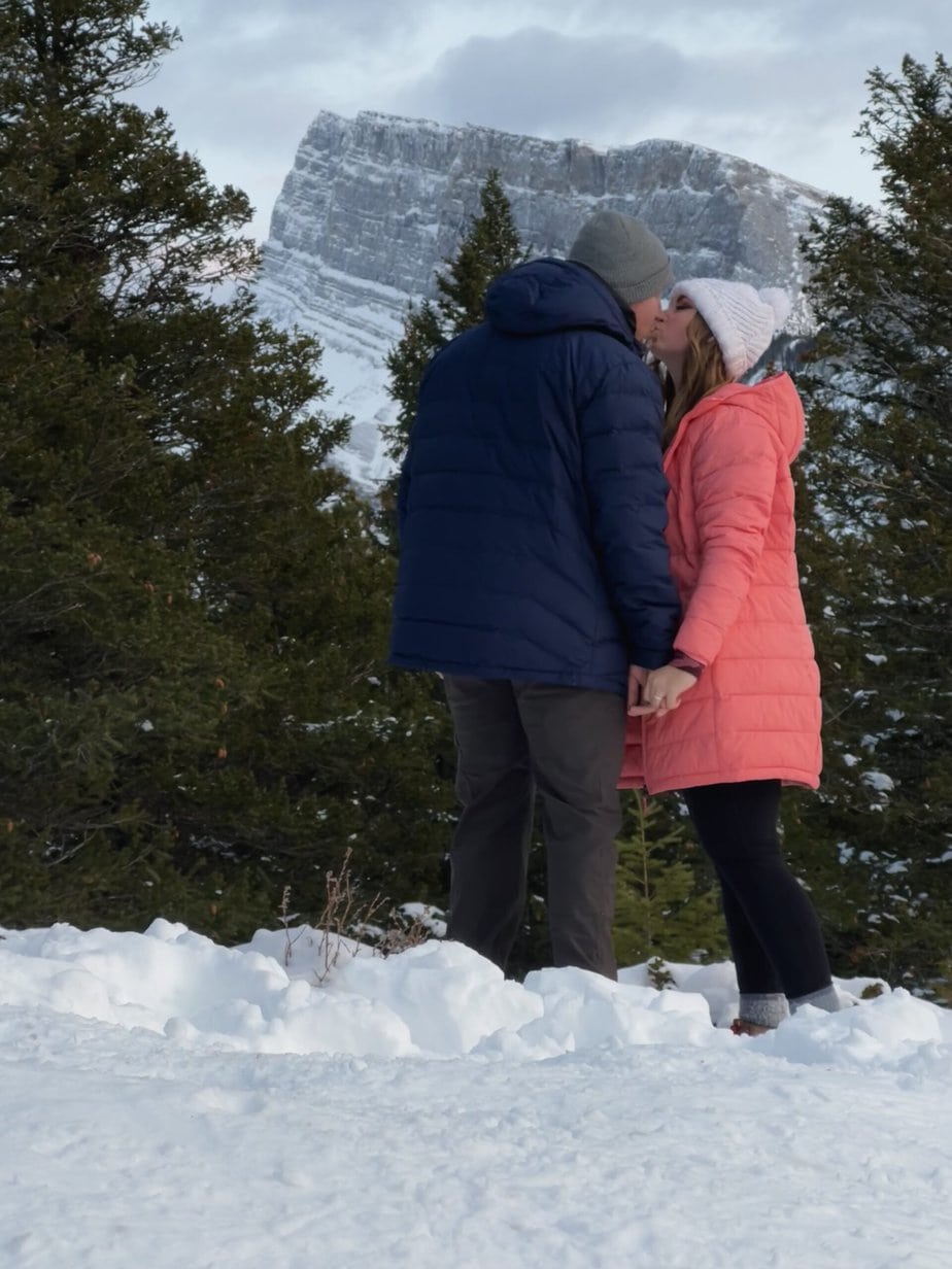 Girl in a Pink Coat Kissing a Boy in a Blue Coat in the Snow