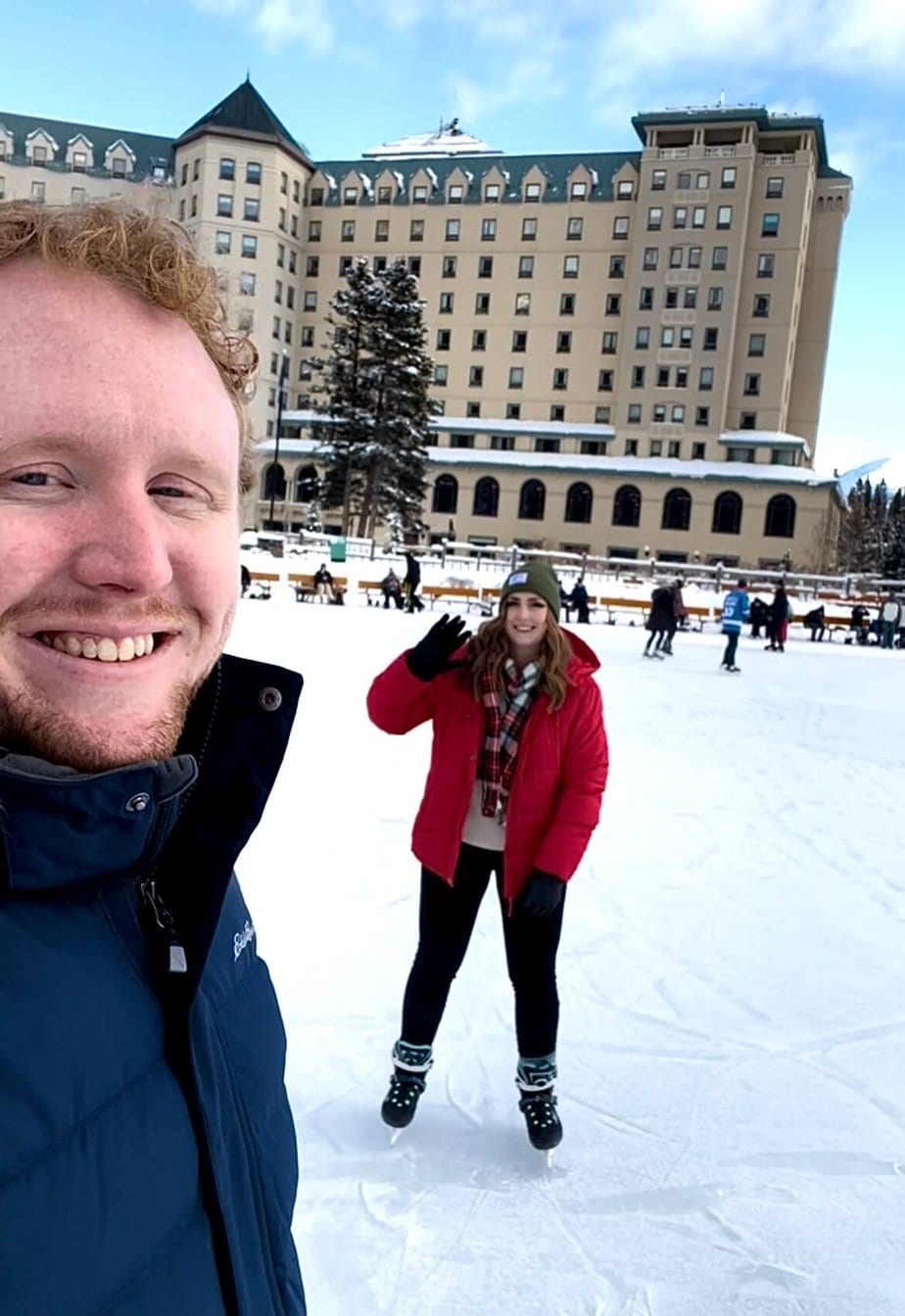 Girl and Guy Standing on a Frozen Lake by a Tall Hotel