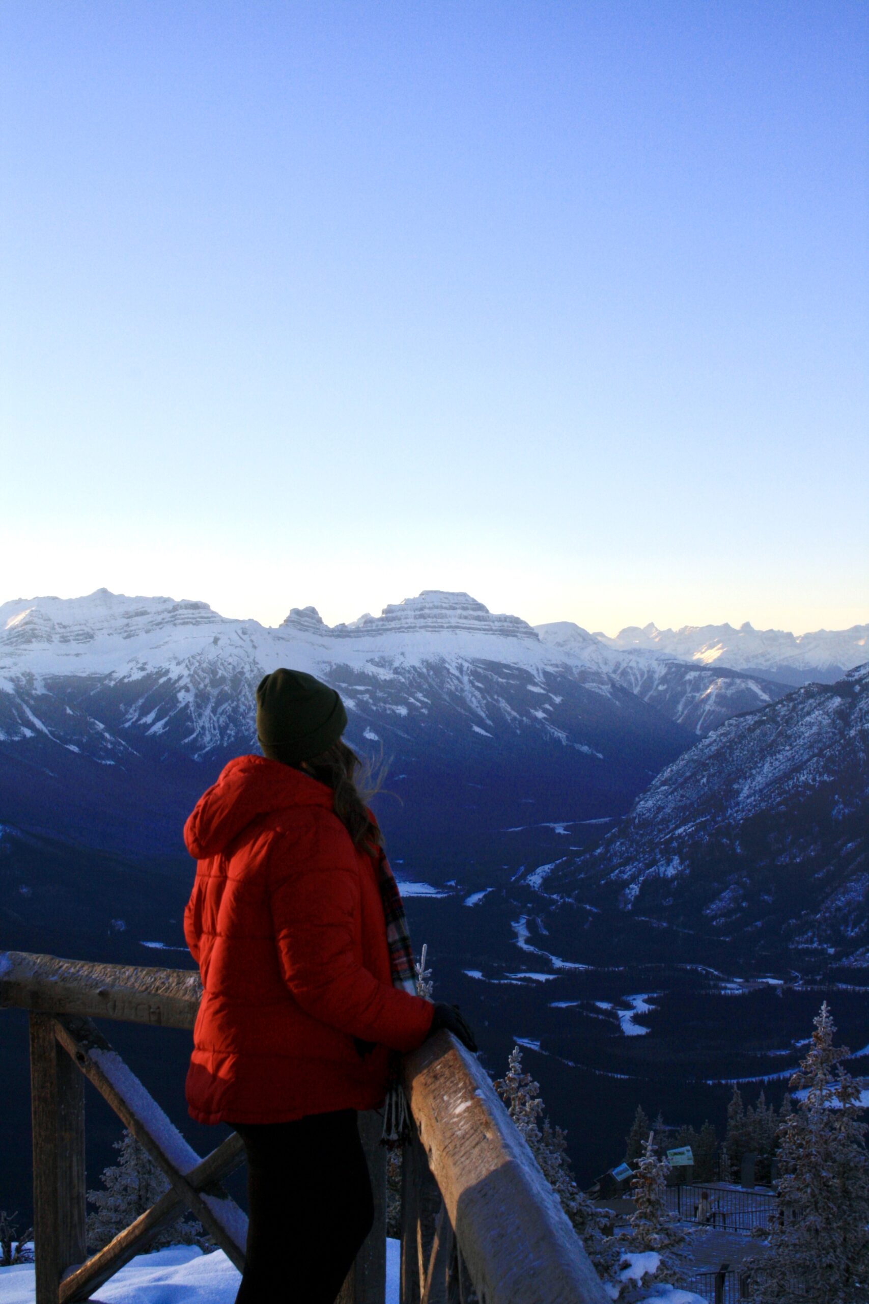 Girl in a Red Coat Holding onto a Wood Rail on top of a mountain