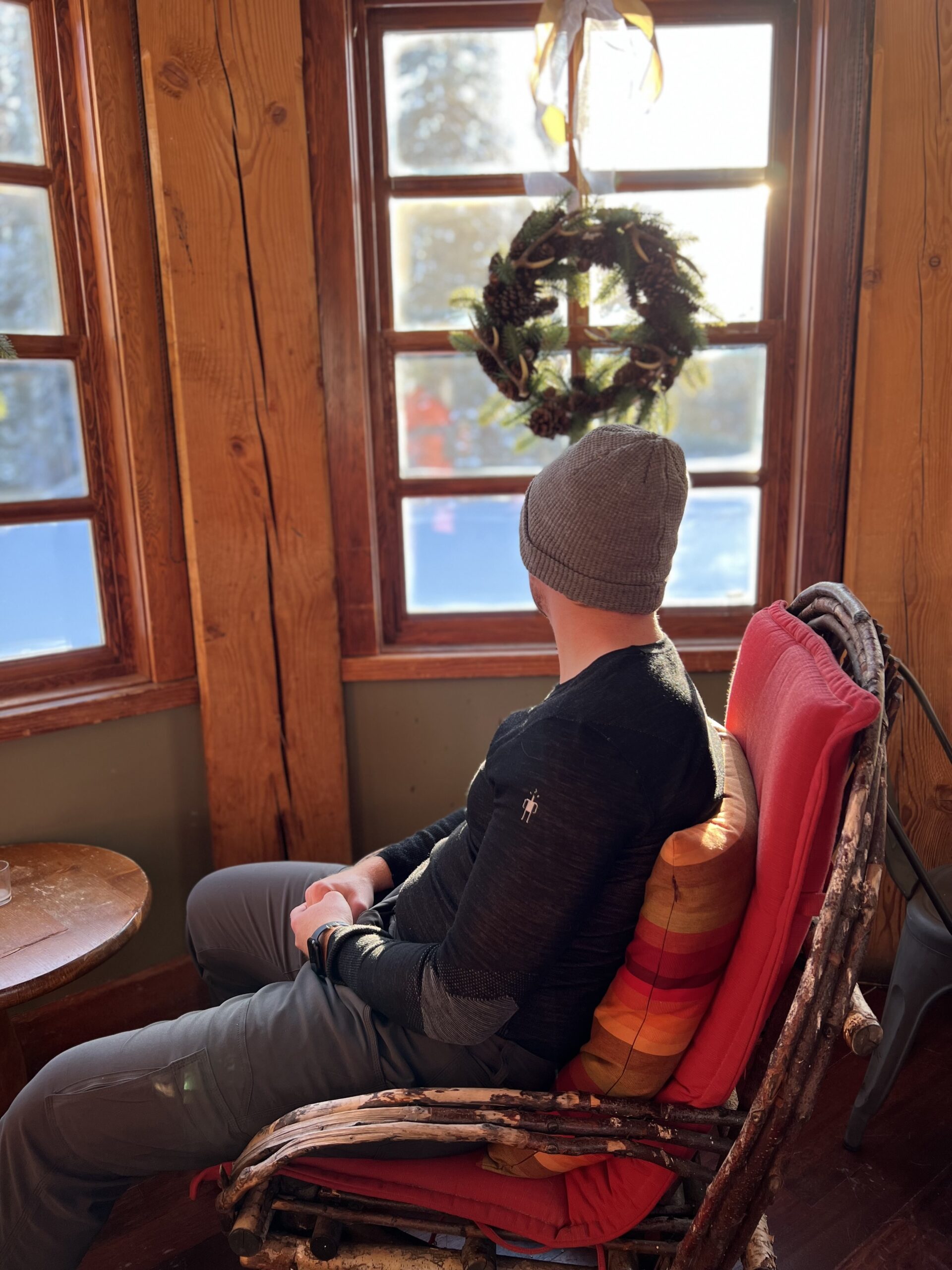 Man in a Gray Beanie and Black Shirt Looking out a Window with a Wreath