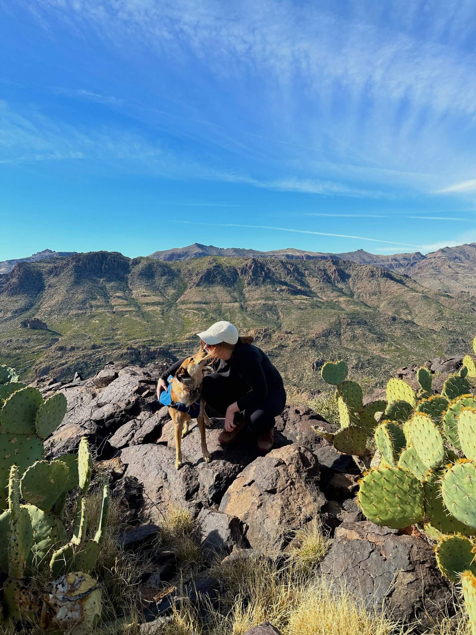 Girl Squatting and Kissing a Dog Outside on a Rock with Cactus Around