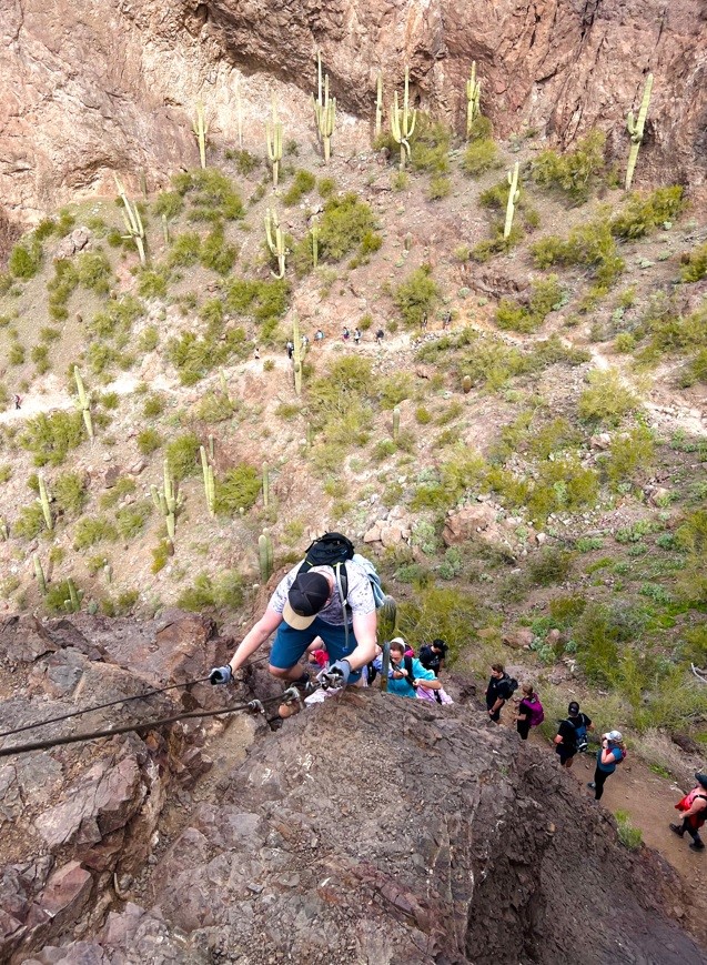 Man in a Hat Climbing with Cables up the Edge of a cliff