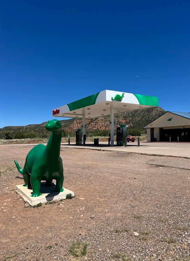 green dinosaur in front of a gas station 
