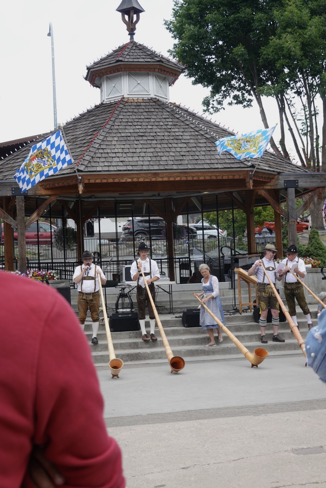 multiple people with german clothing playing a large horn under a gazebo