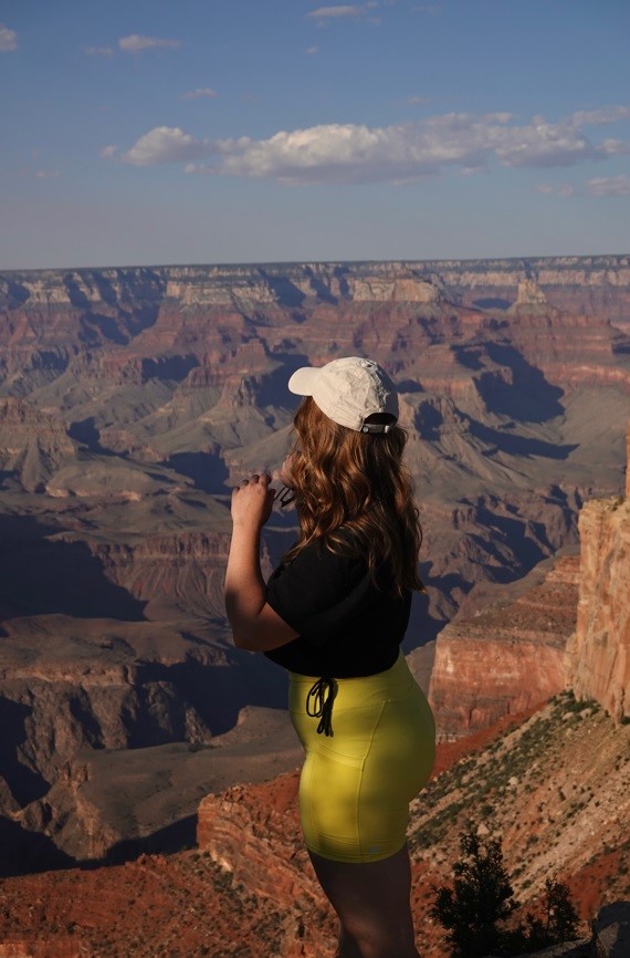 girl with curly hair and a black shirt and yellow shorts in front of a canyon