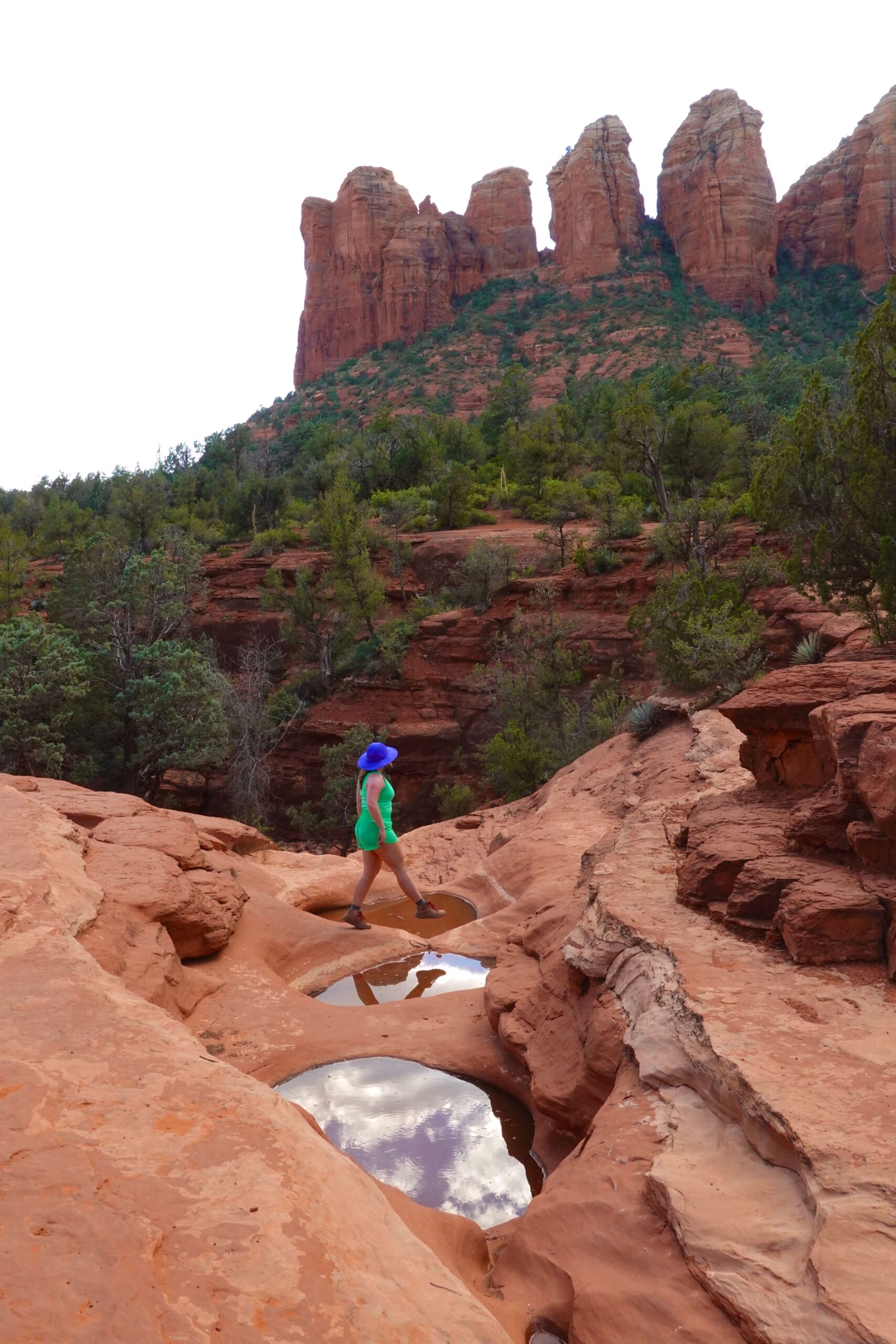 girl wearing green and blue stepping over a red rock pool of water