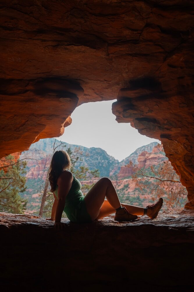 girl sitting in a cave overlooking red rock