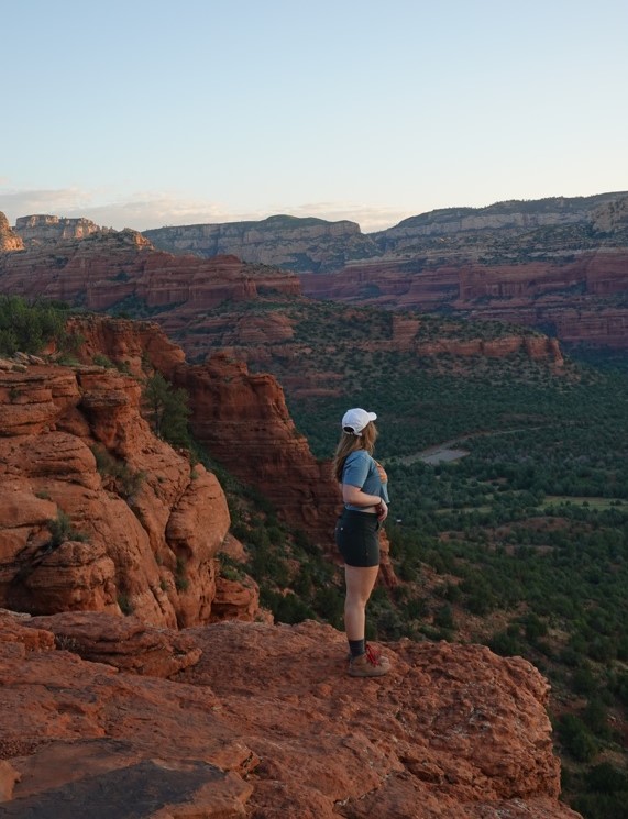 girl standing to the side looking over a cliff of red rock