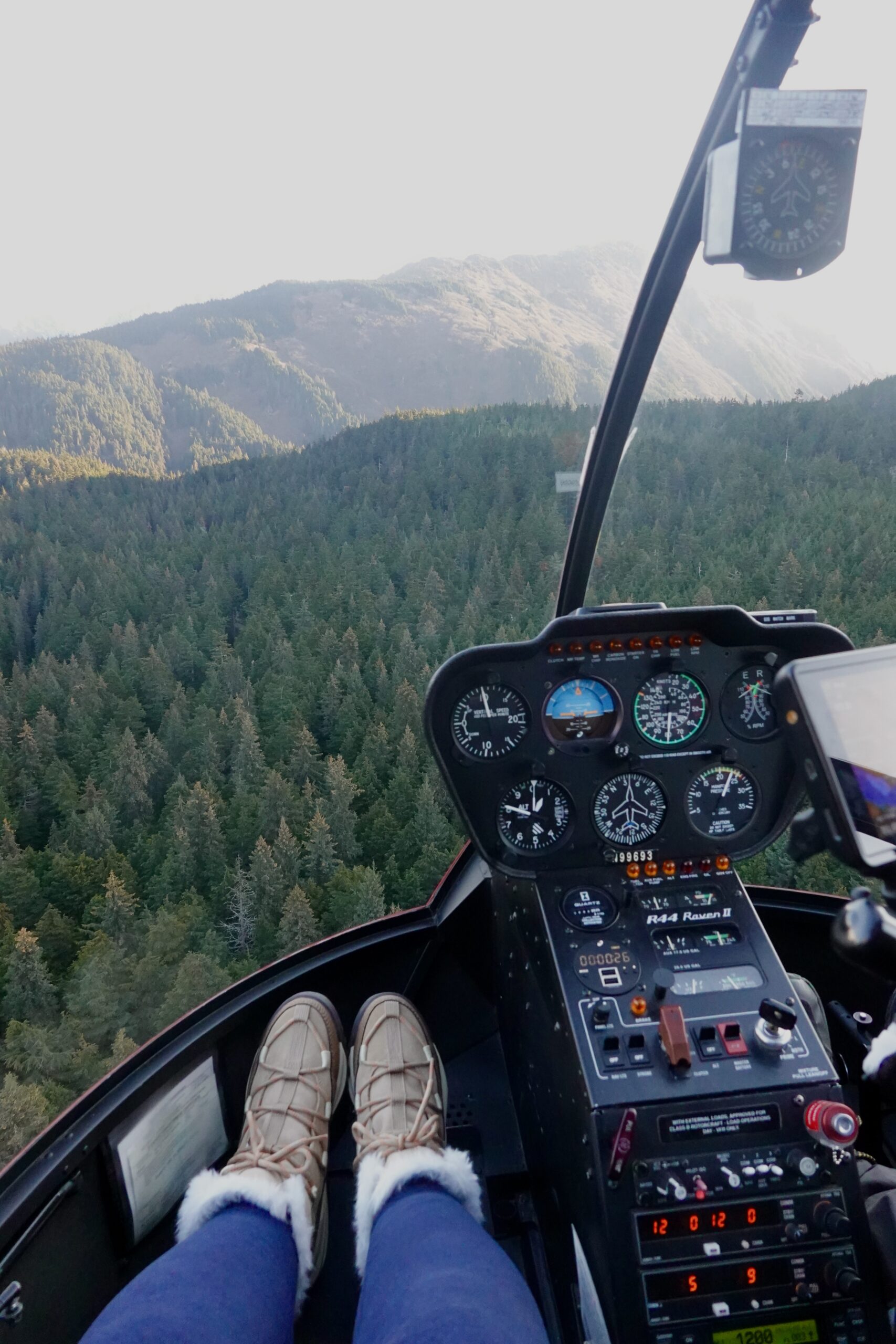 girl in boots sitting in a helicopter over pine trees