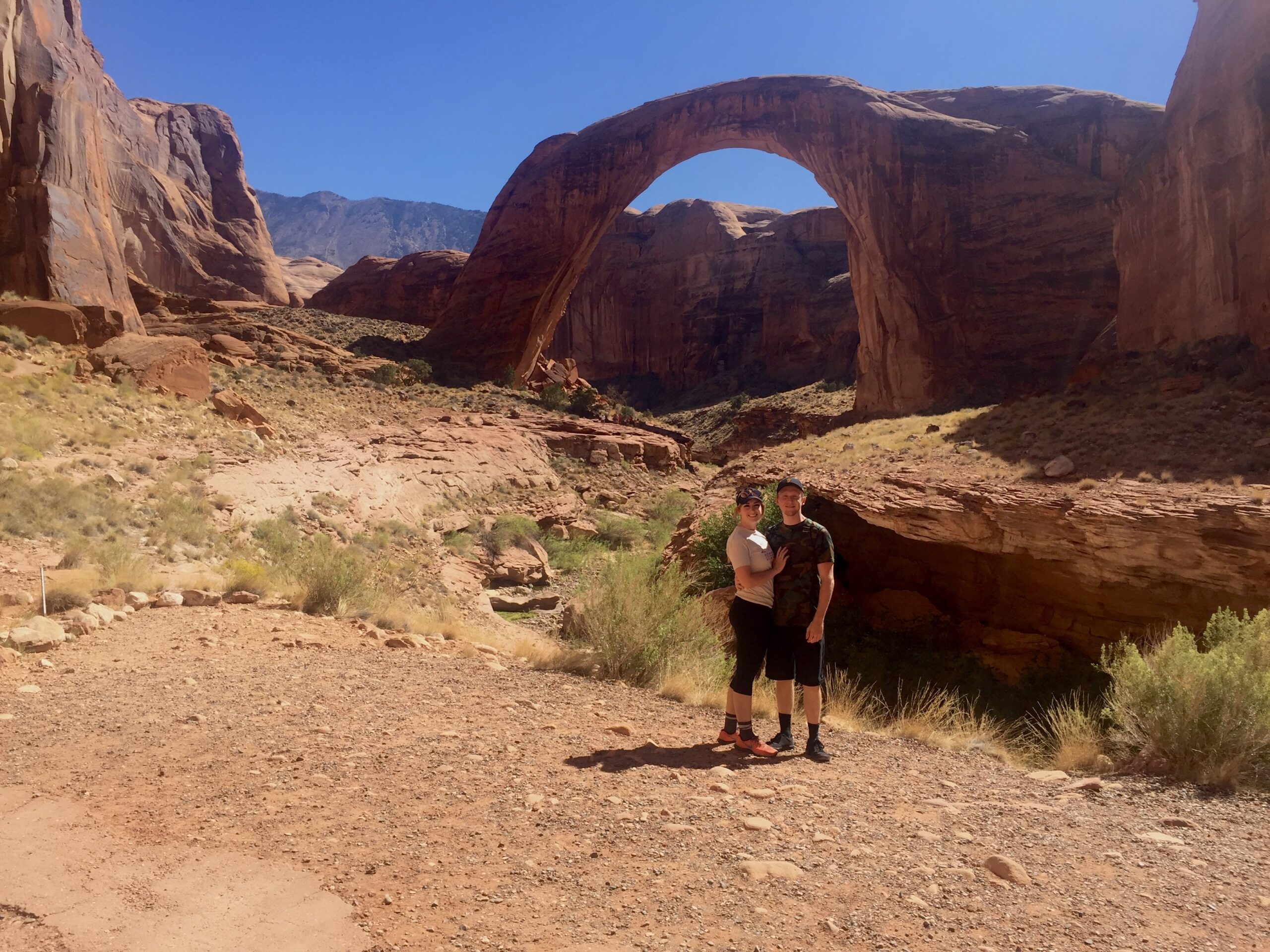 arch bridge in the desert with two people in front of it