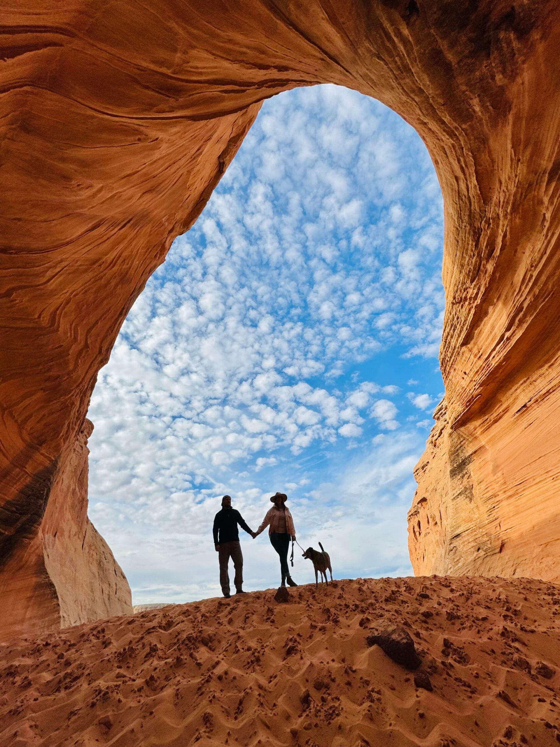 two people holding hands with a dog in a cave