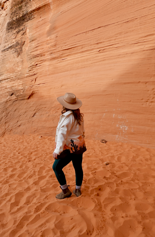girl standing in sand in front of red rock