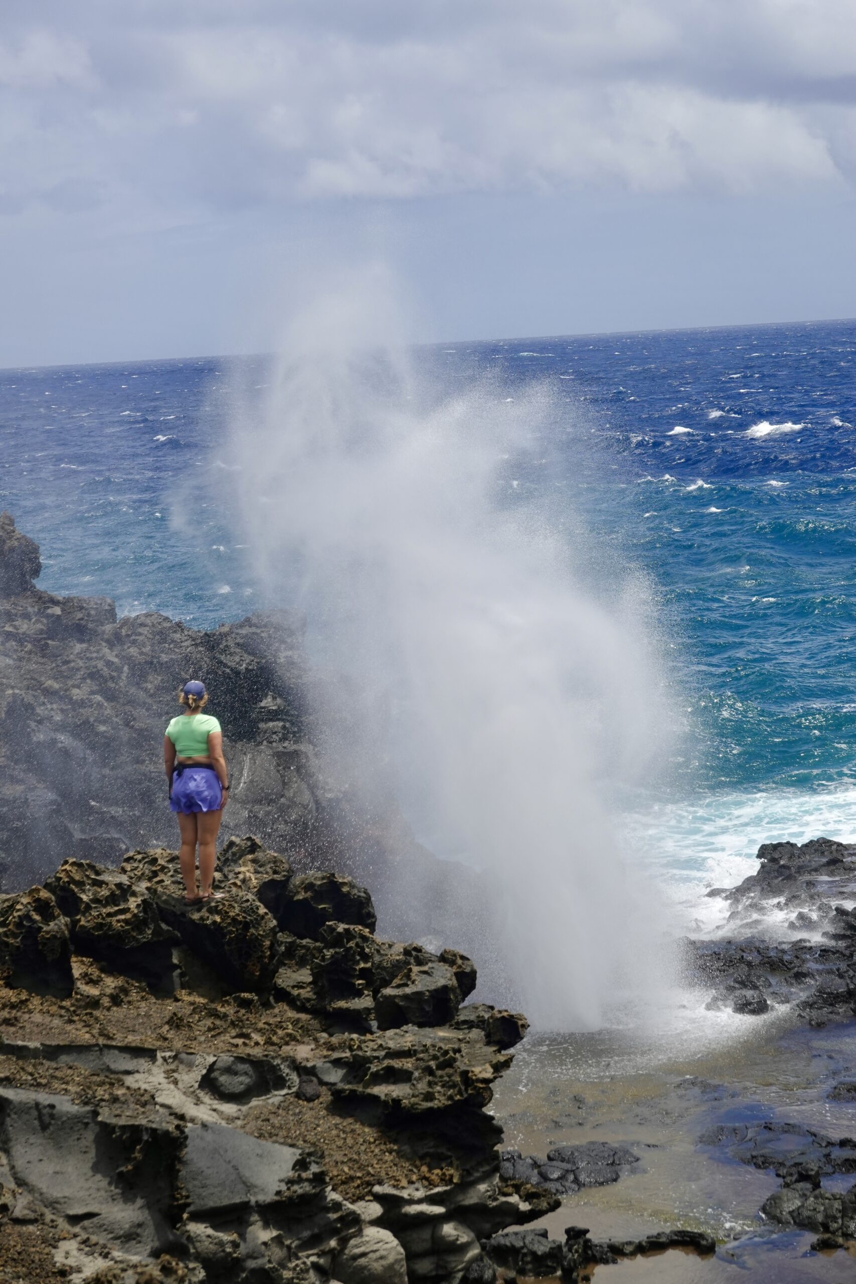 girl in blue and green standing by a blowhole in maui