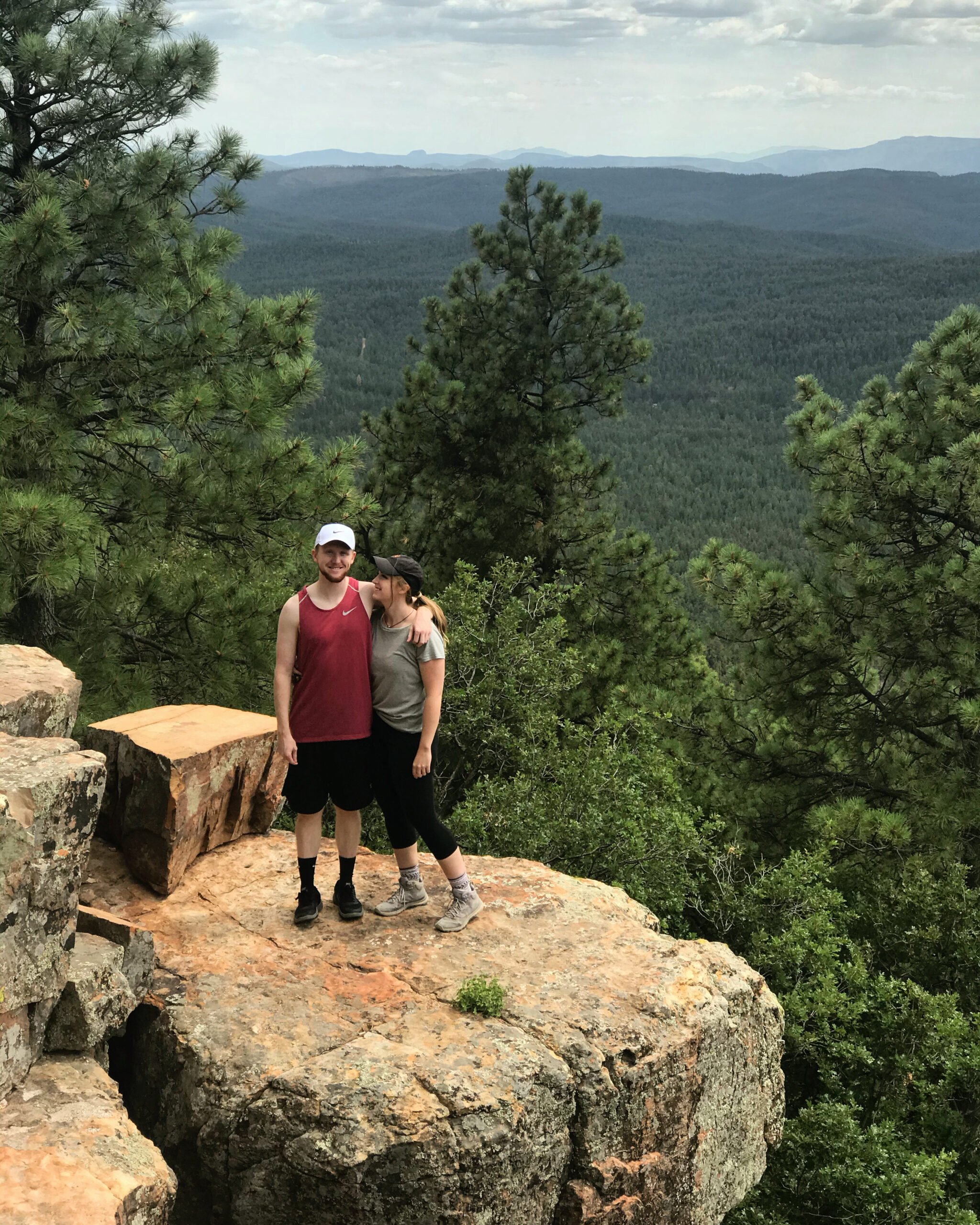 couple standing on a rock overlooking a forest of trees