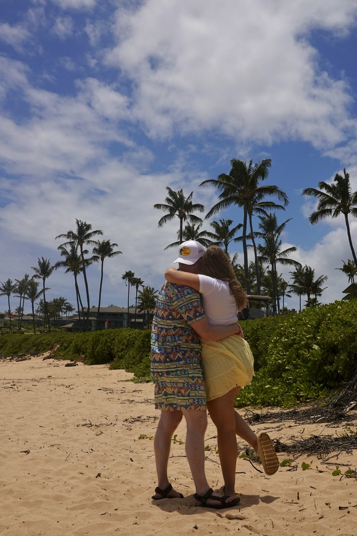 two people hugging on the beach with palm trees