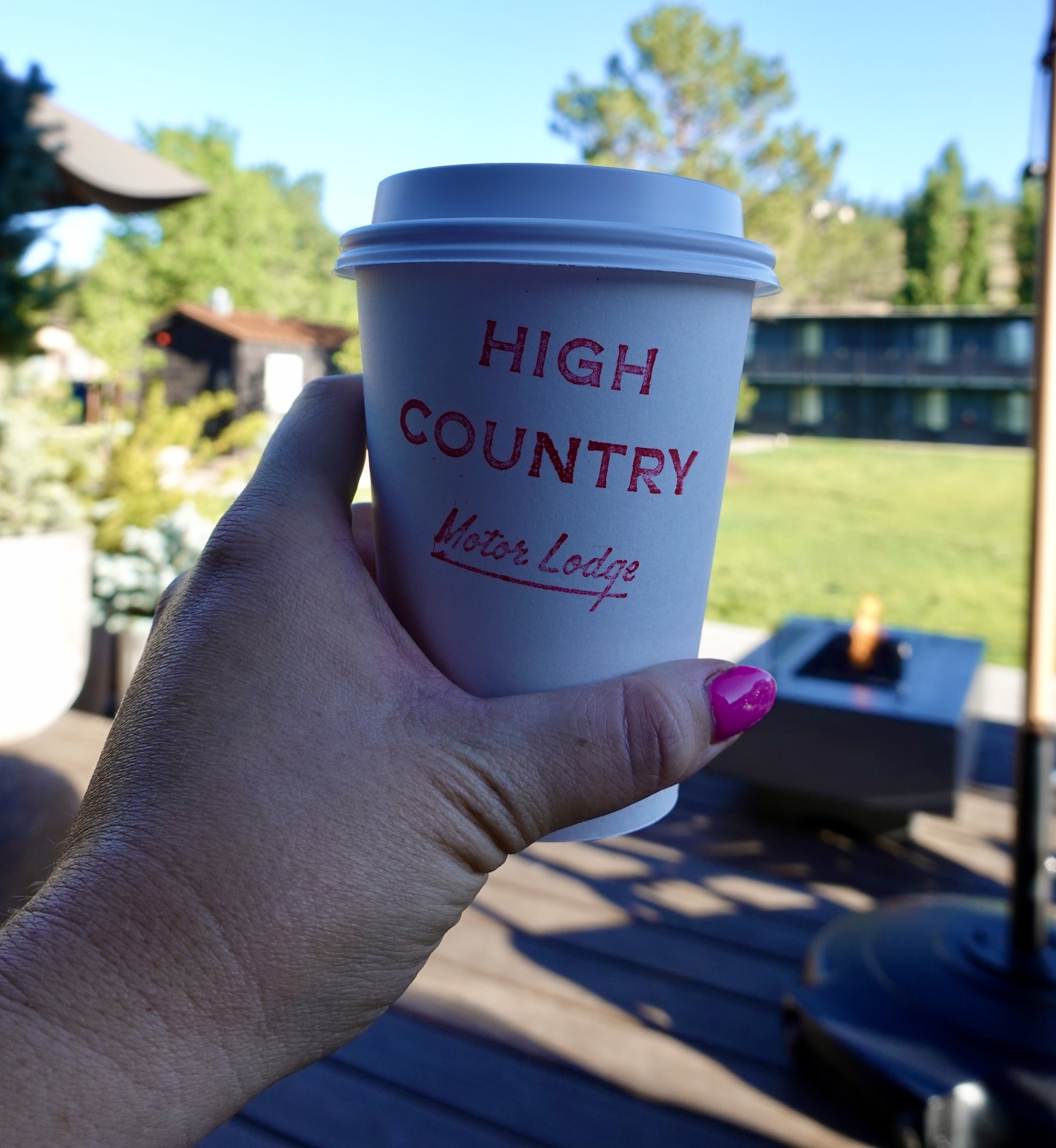 girl holding a coffee cup reading high country motor lodge