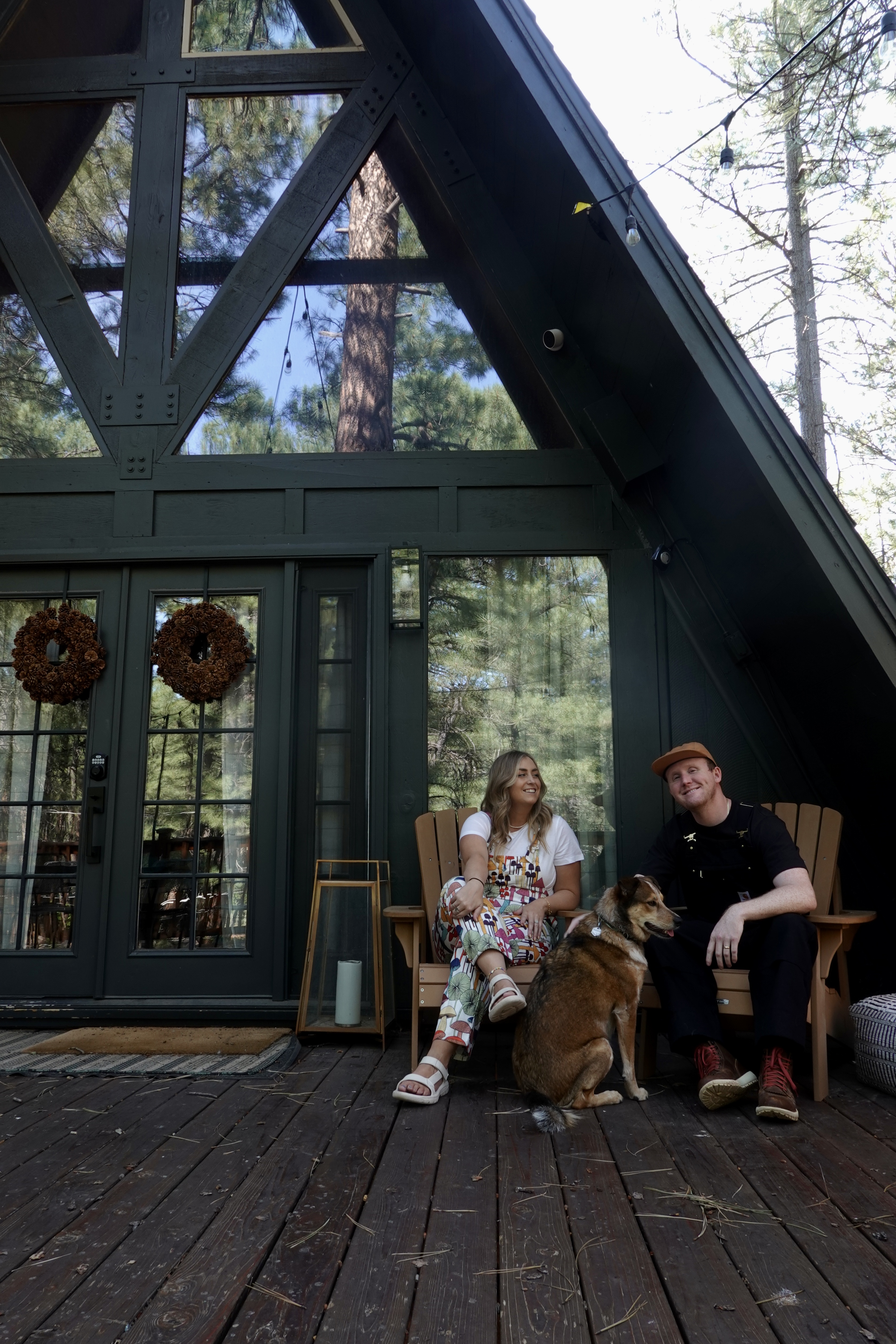 girl and boy and dog sitting on a chair in front of a black a frame cabin