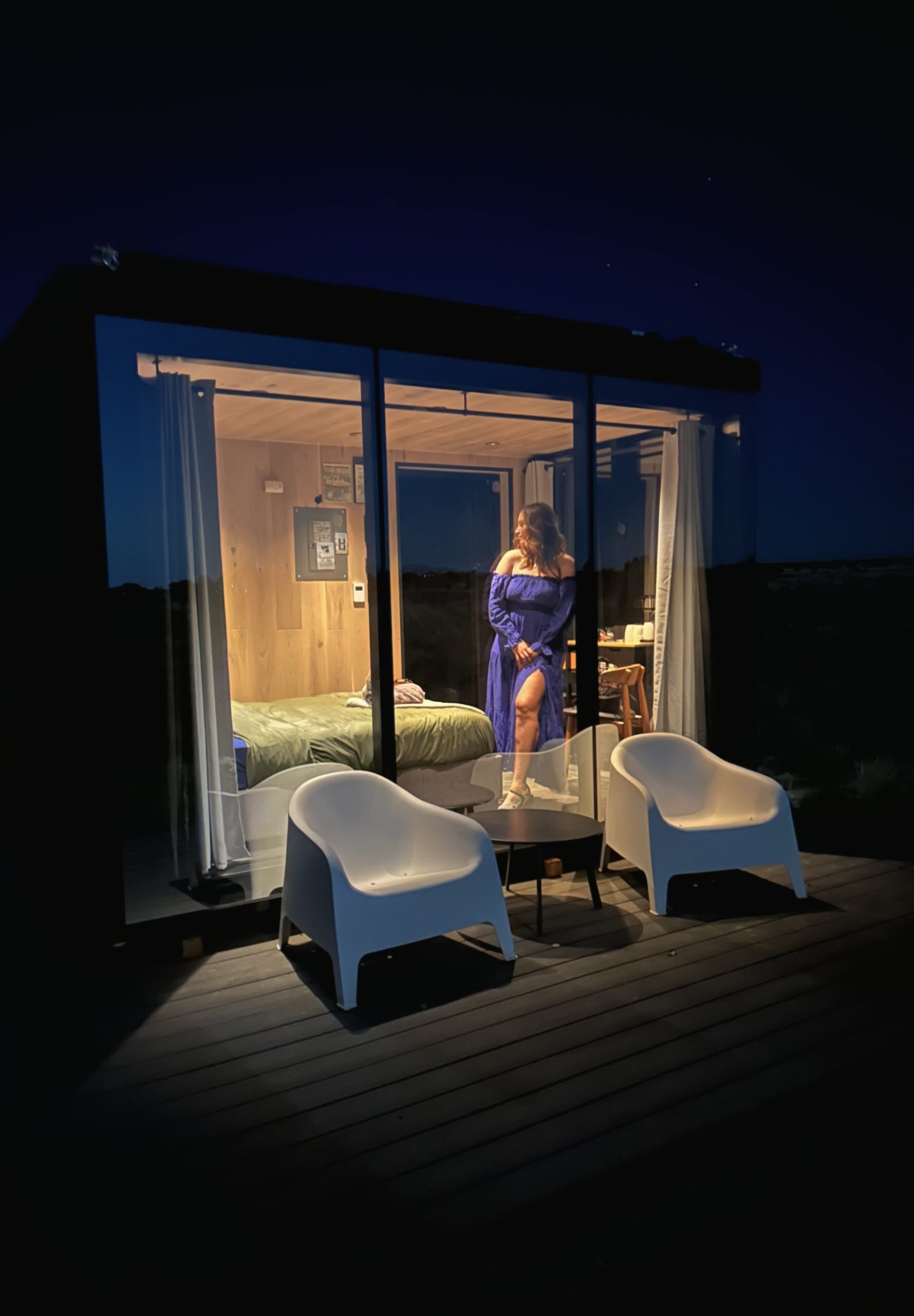 photo of a glass house at night with a girl standing