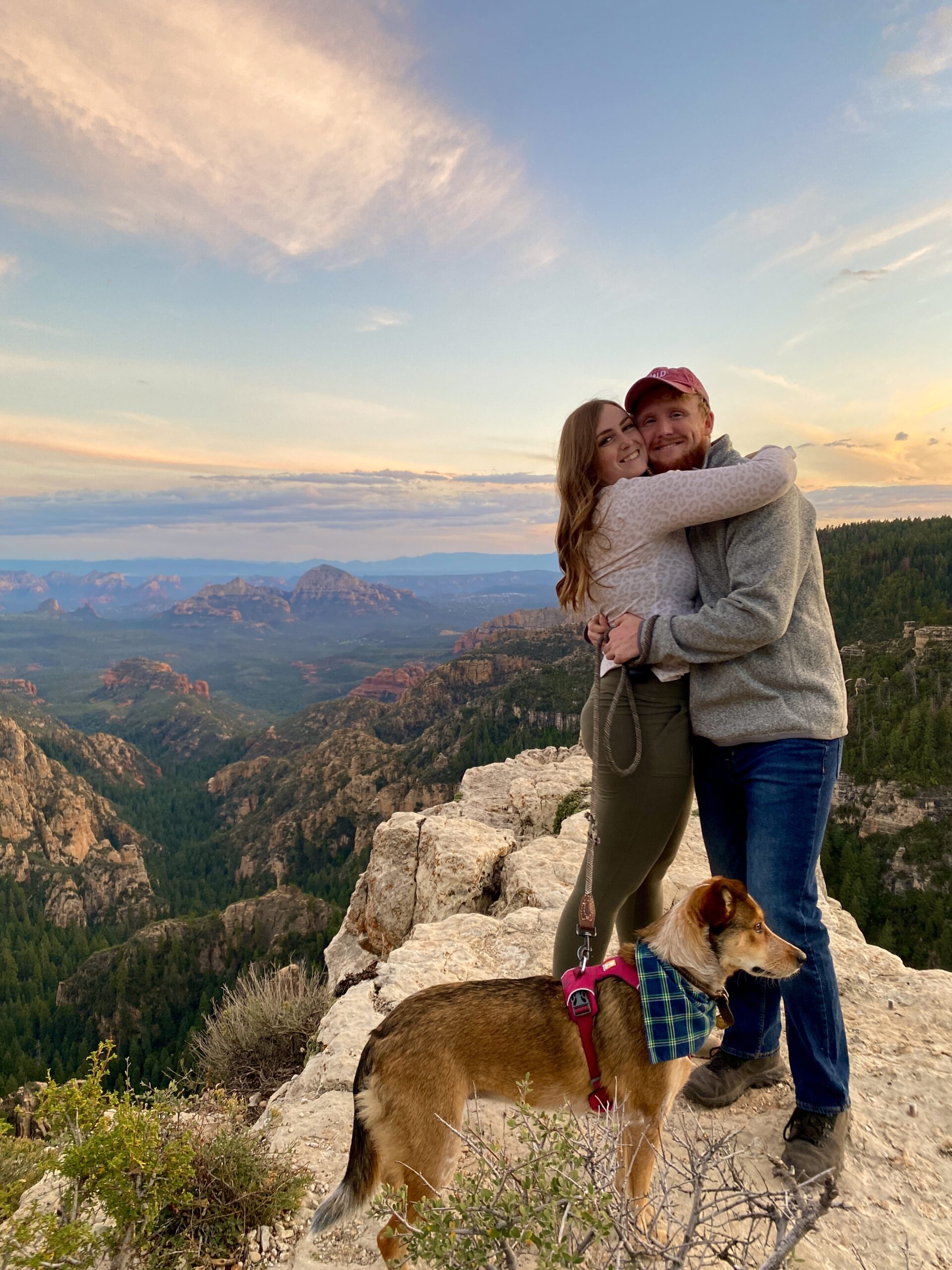 couple with a dog hugging each other during sunset