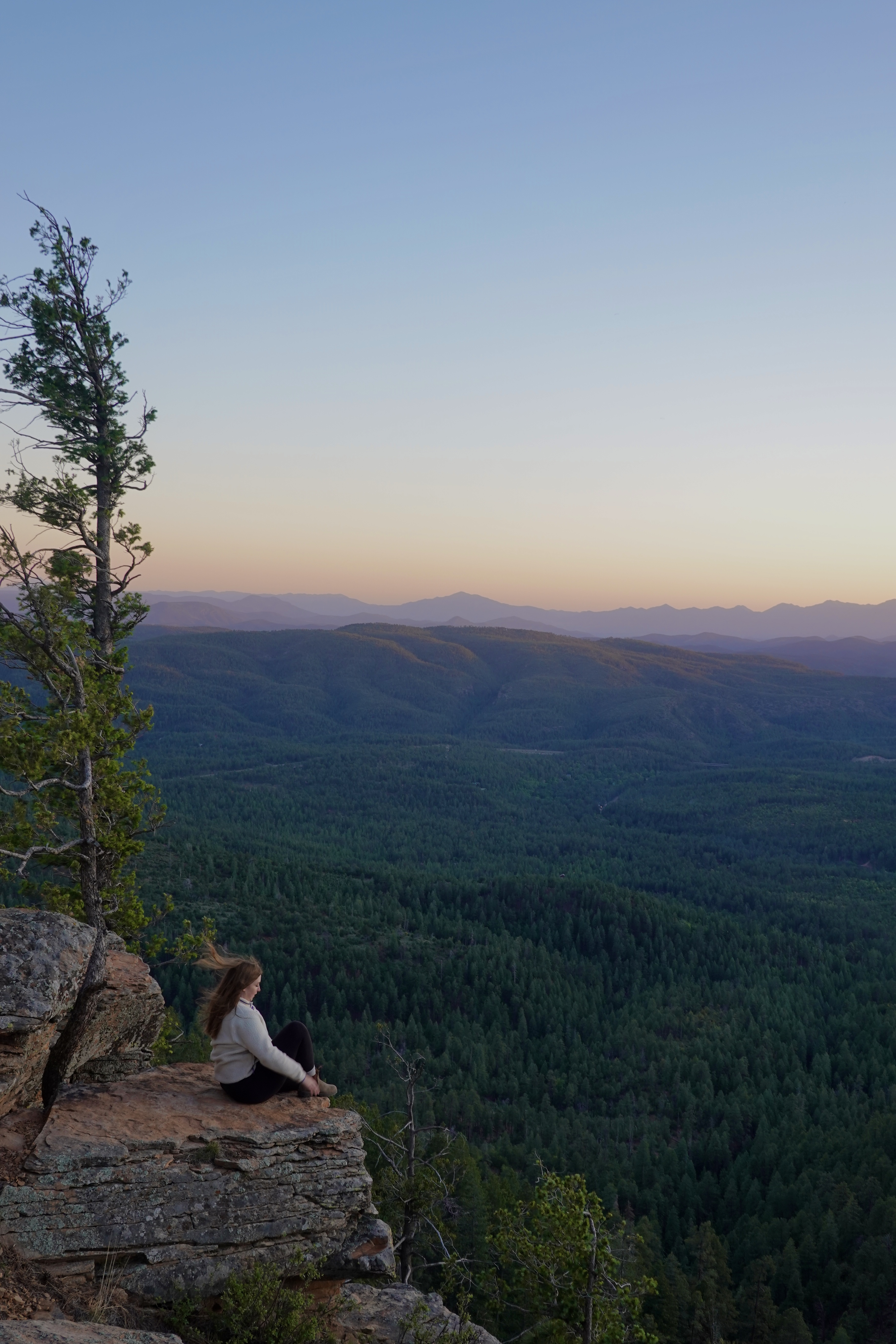 girl sitting on a rock ledge at sunset