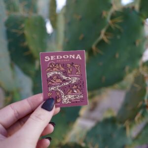 Hand holding a maroon card with a map of Sedona, Arizona in front of a cactus.