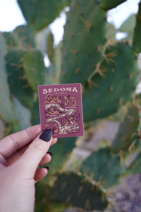 Hand holding a maroon card with a map of Sedona, Arizona in front of a cactus.