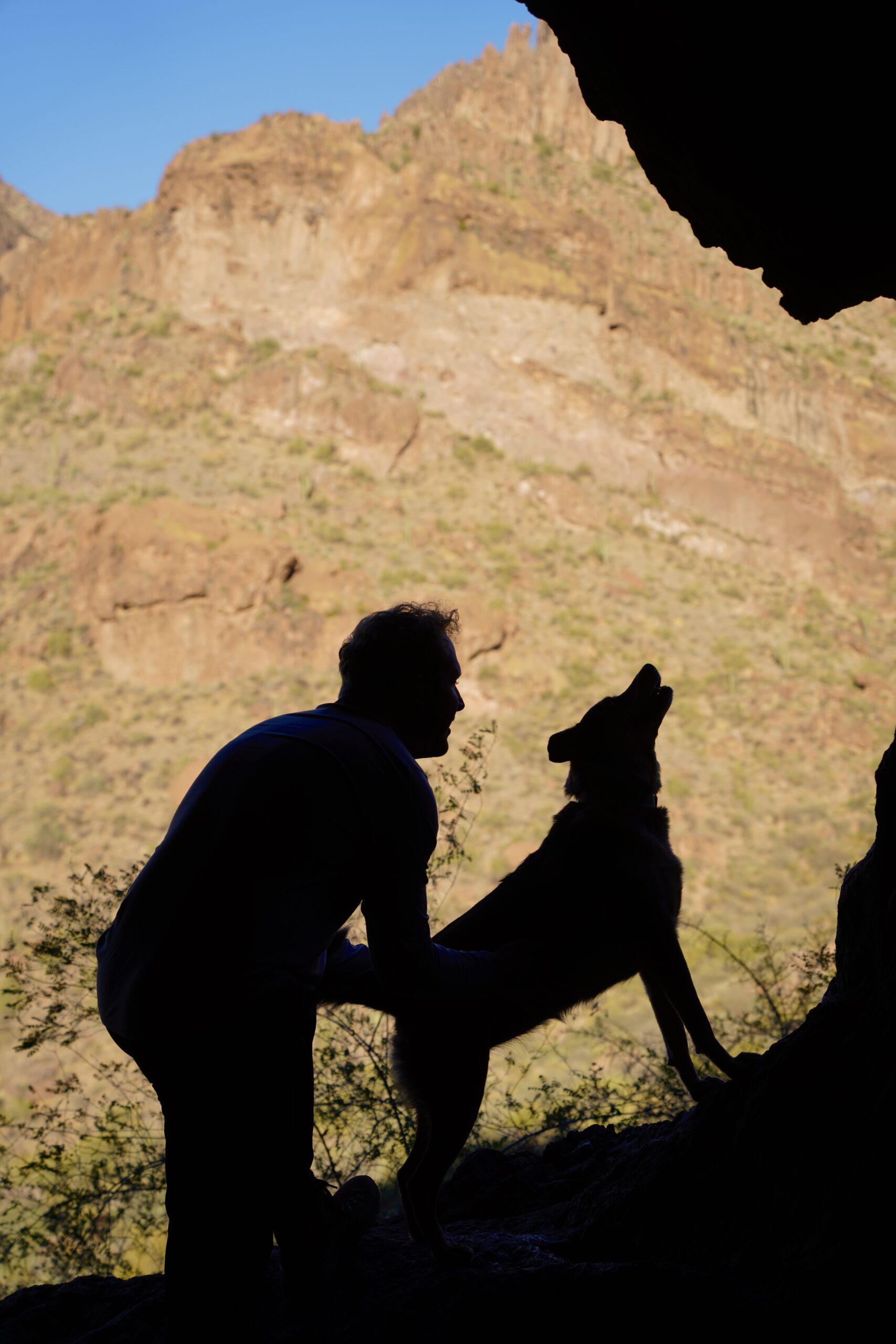 outline of a man and a dog looking up, in a cave in the mountains