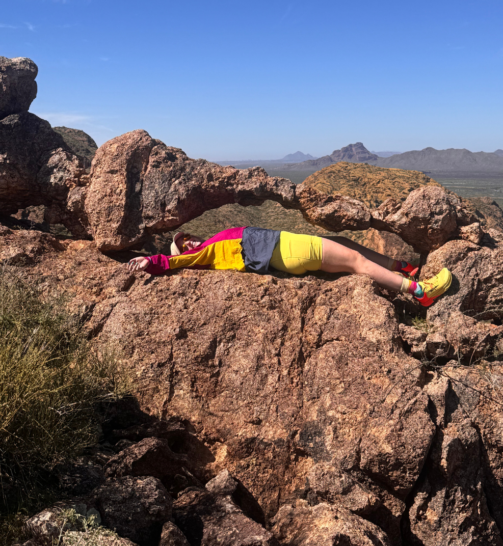 girl in colorful clothes laying under an arch made of rock