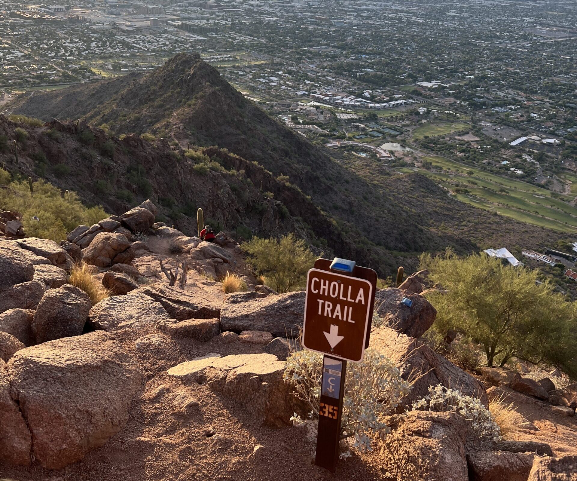 photo of a mountain at sunrise with a sign with an arrow saying cholla trail