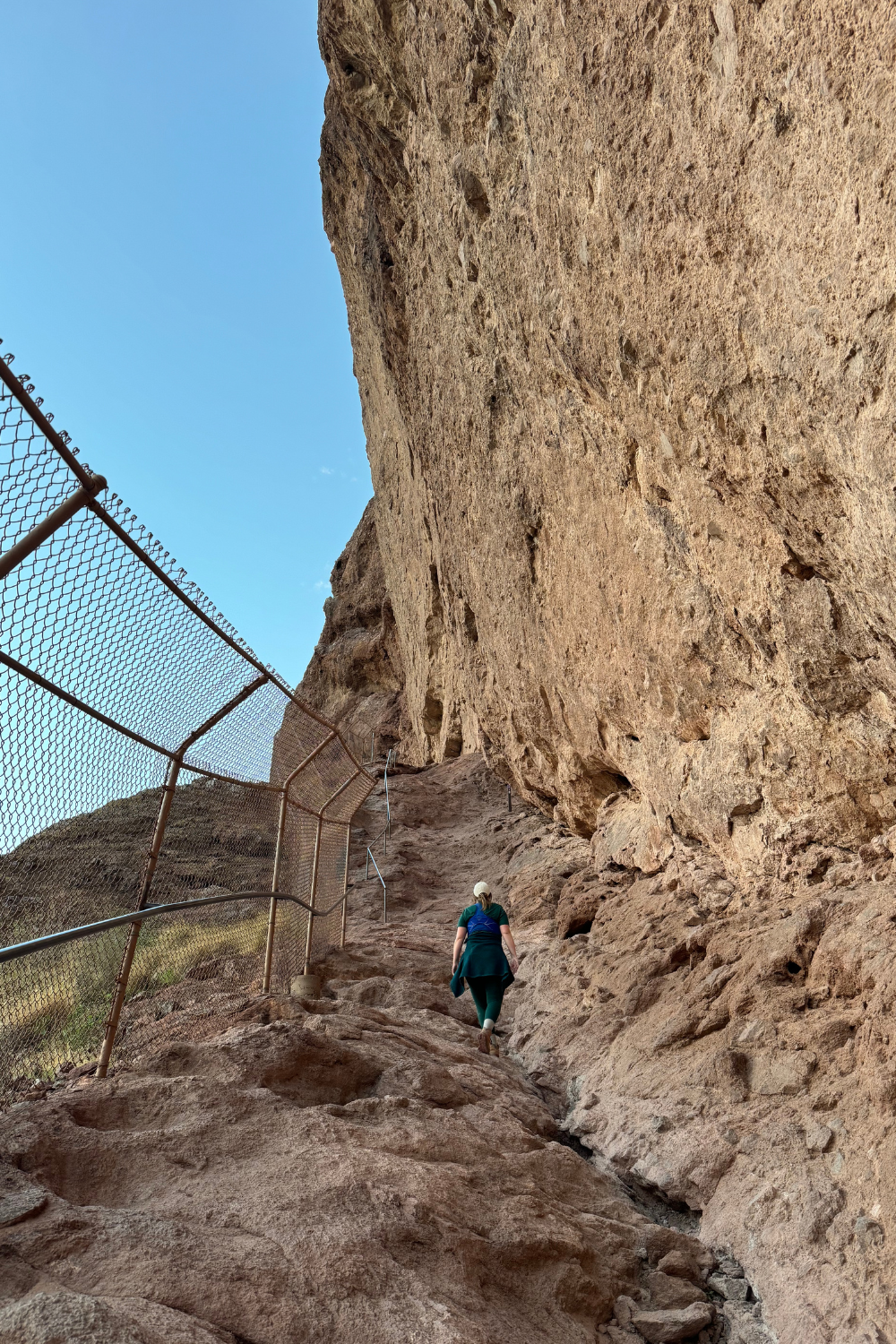 girl hiking up a mountain that has a cage on one side and mountain on another