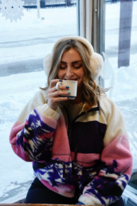 girl sipping coffee with a pink blue and white fleece on