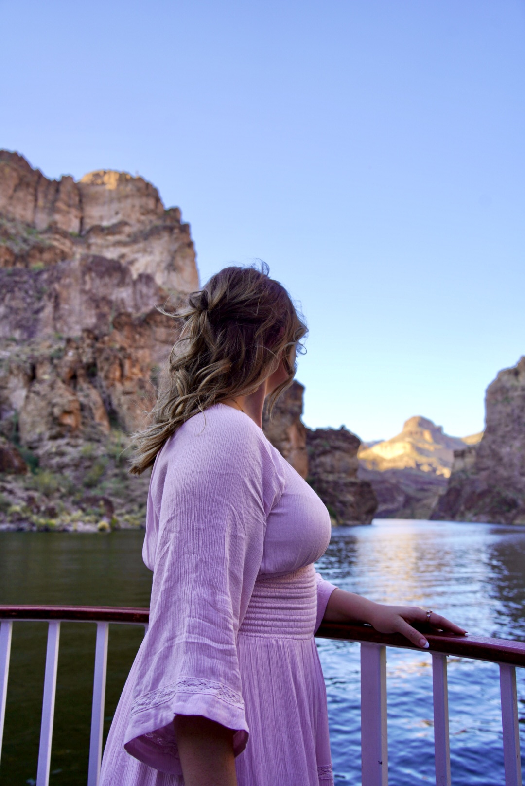 canyon girl in a purple dress standing on a boat overlooking water and a rugged desert landscape in arizona