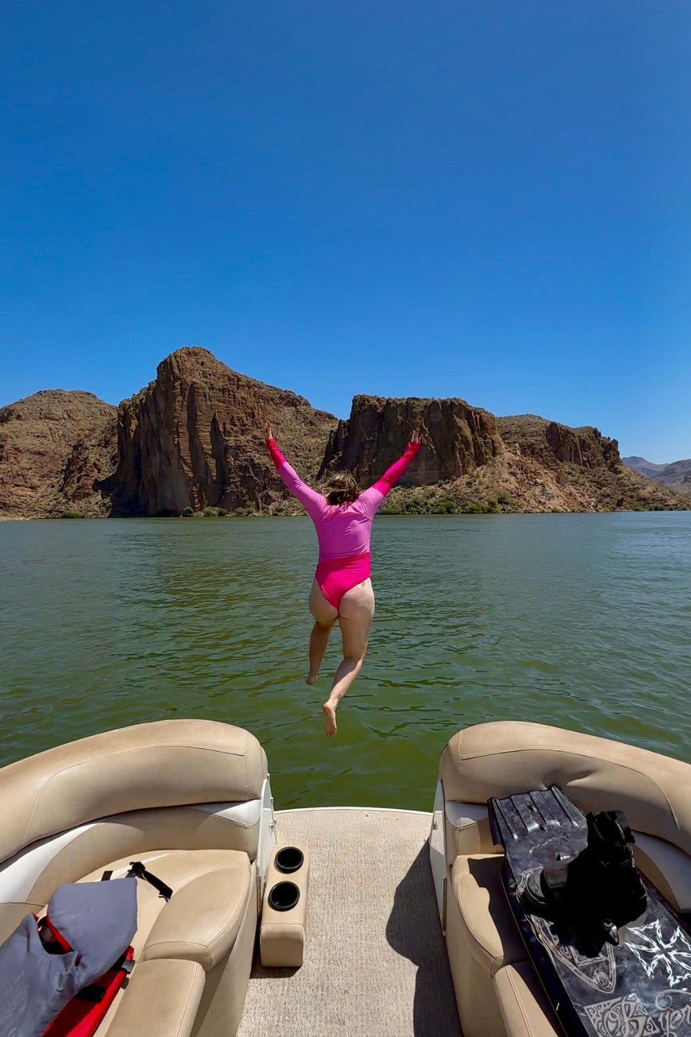 jumping into canyon lake girl in a pink bathing suit jumping into a lake surrounded by desert mountains