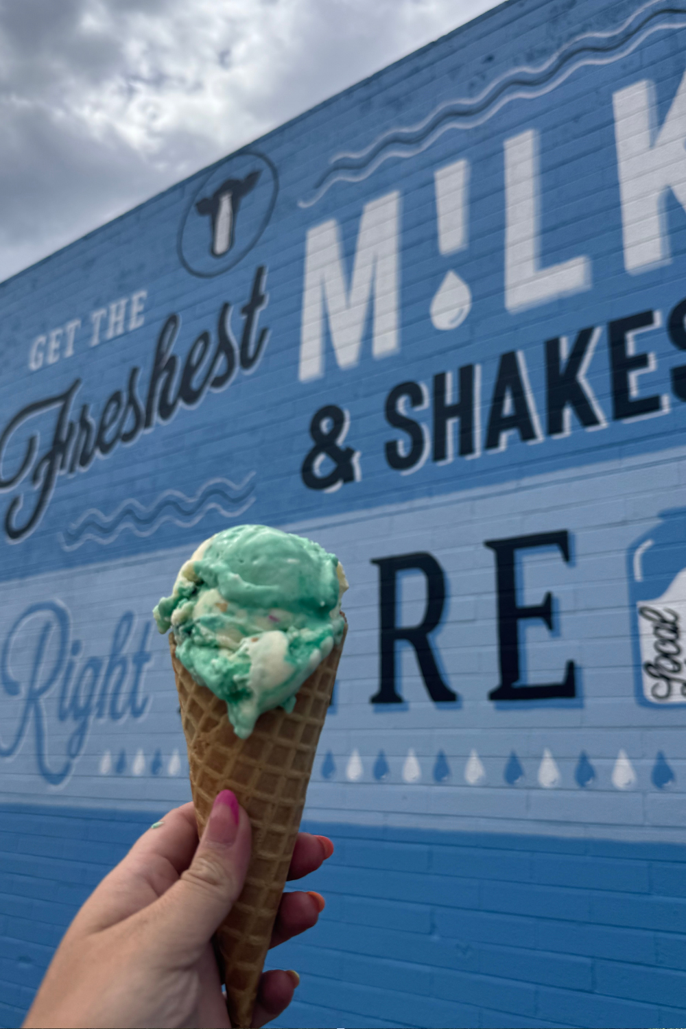 photo of a girl holding up an ice cream cone in front of a mural