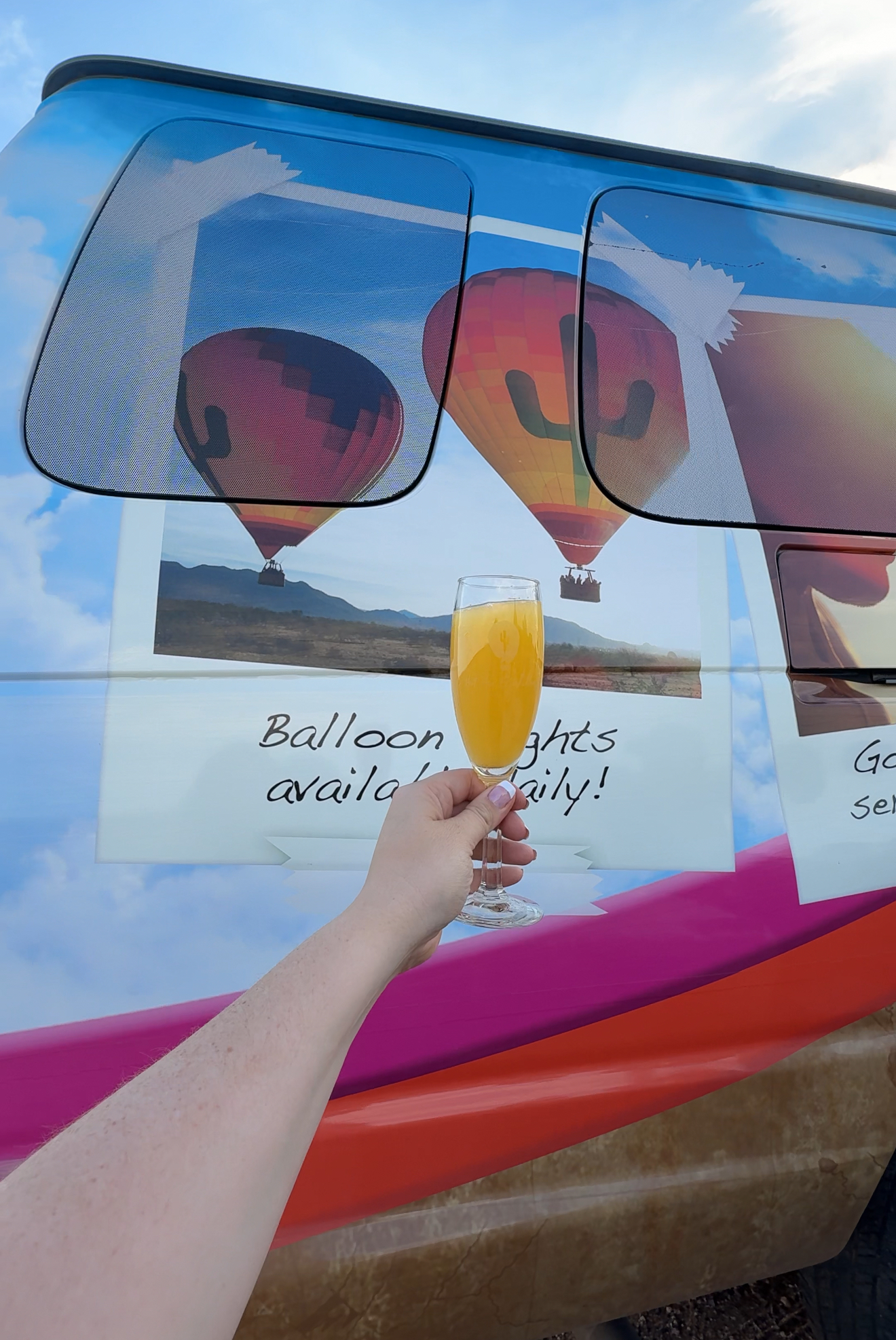 photo of a girl holding up a mimosa in front of a van with hot air balloon on it