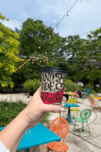 photo of a girl holding up a hot coffee at an outdoor cafe