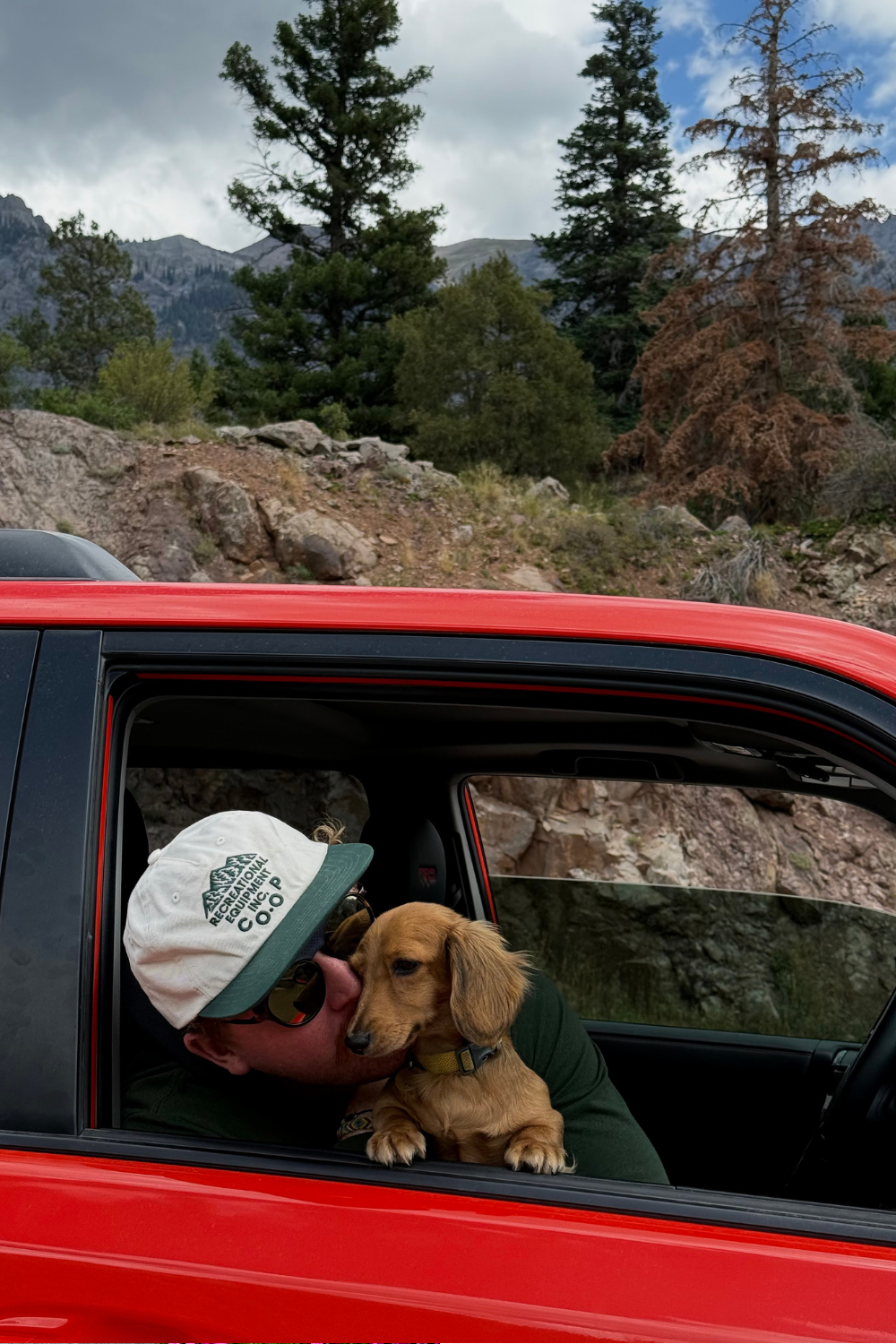 man and little dog in an orange car on the million dollar highway