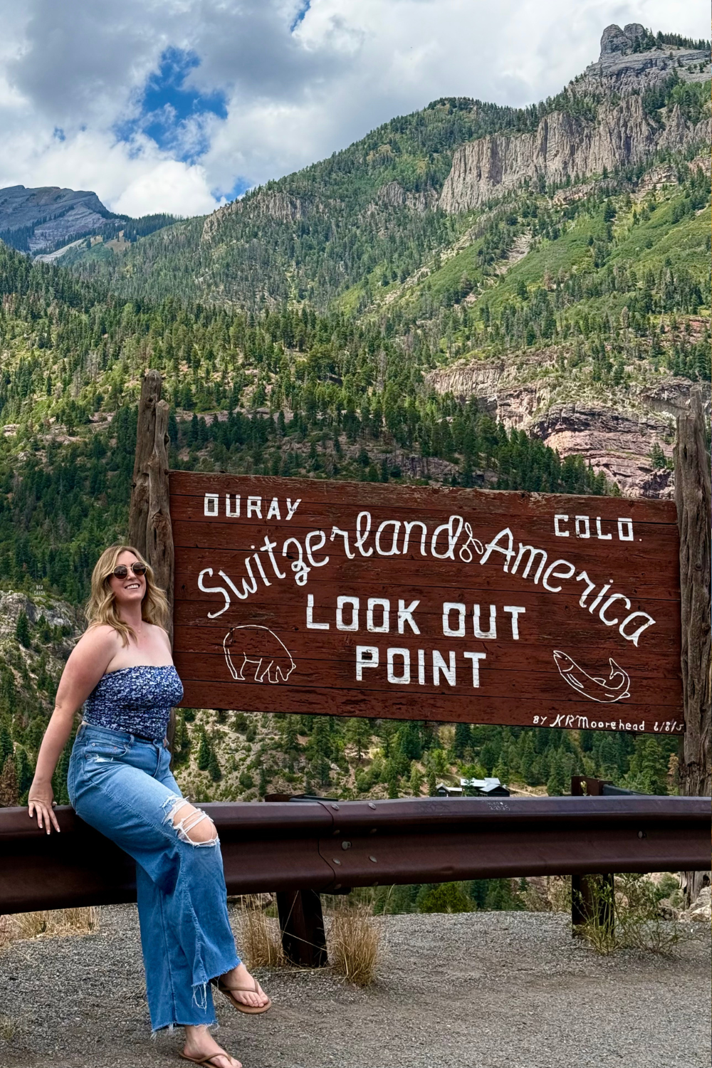 girl sitting by a sign reading "switzerland of america"