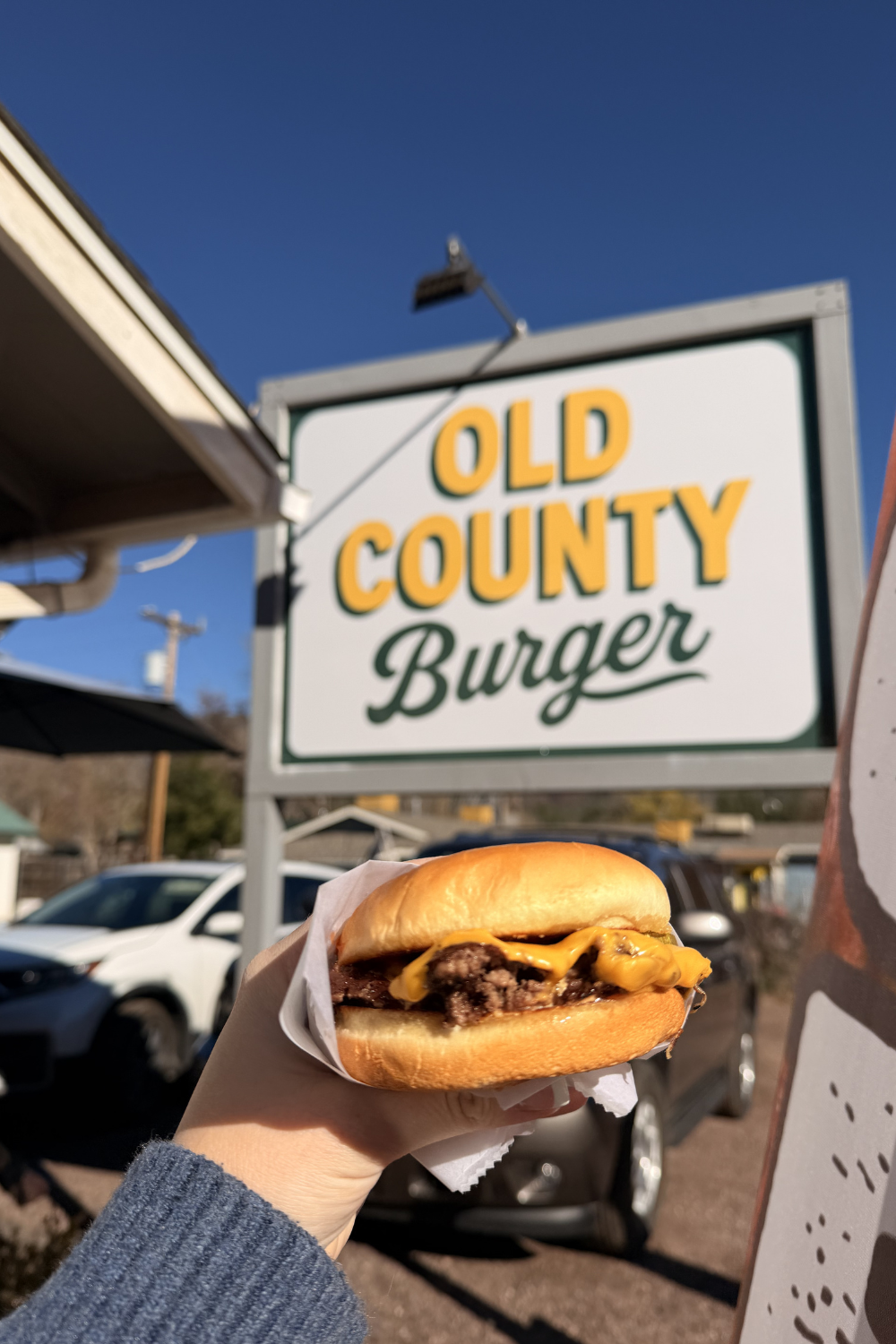 girl holding up a burger in front of a sign reading old county burger