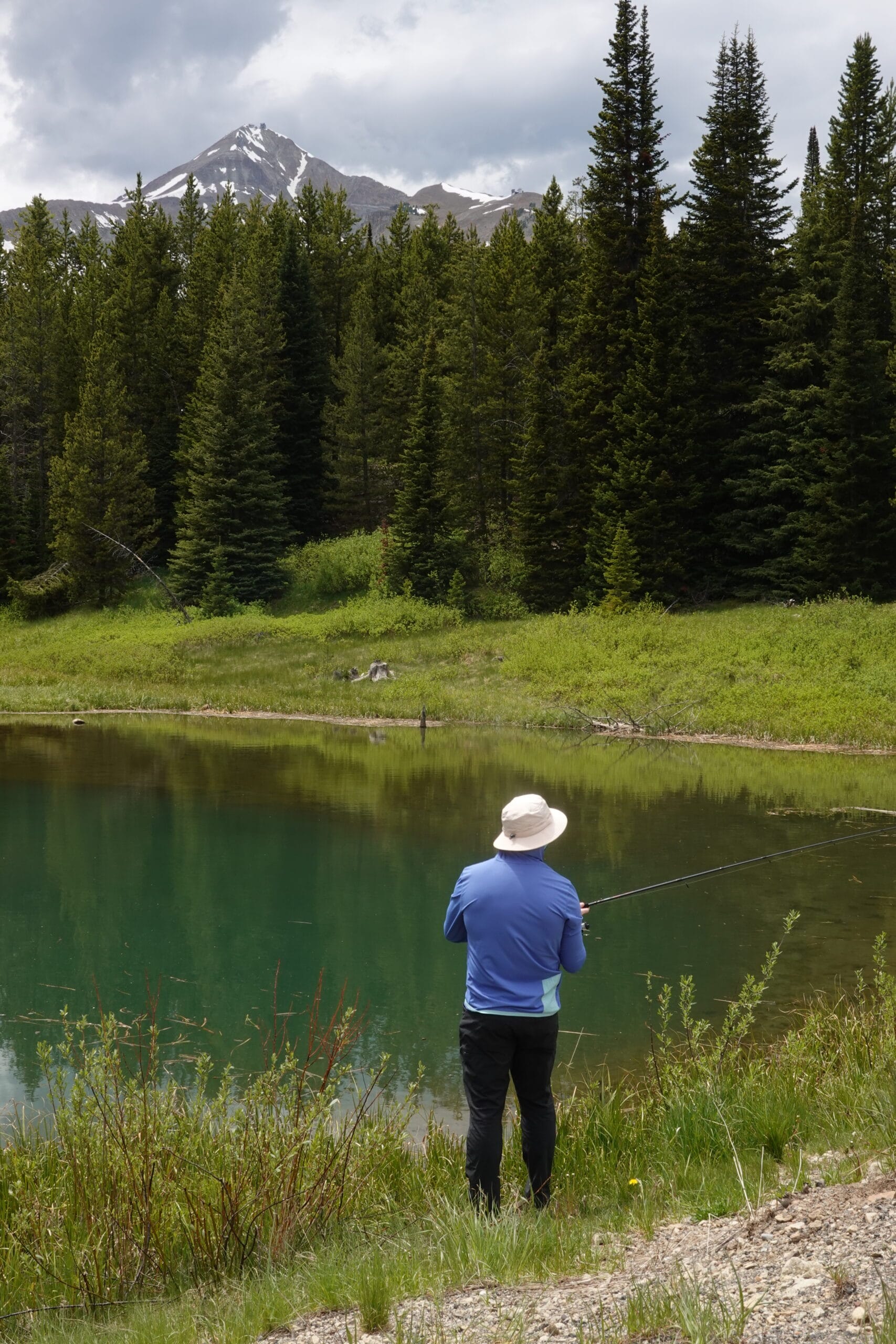 man in blue sun hoodie and wide brim hat fishing in a pond