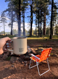 girl holding mug in front of a fire and a camp chair