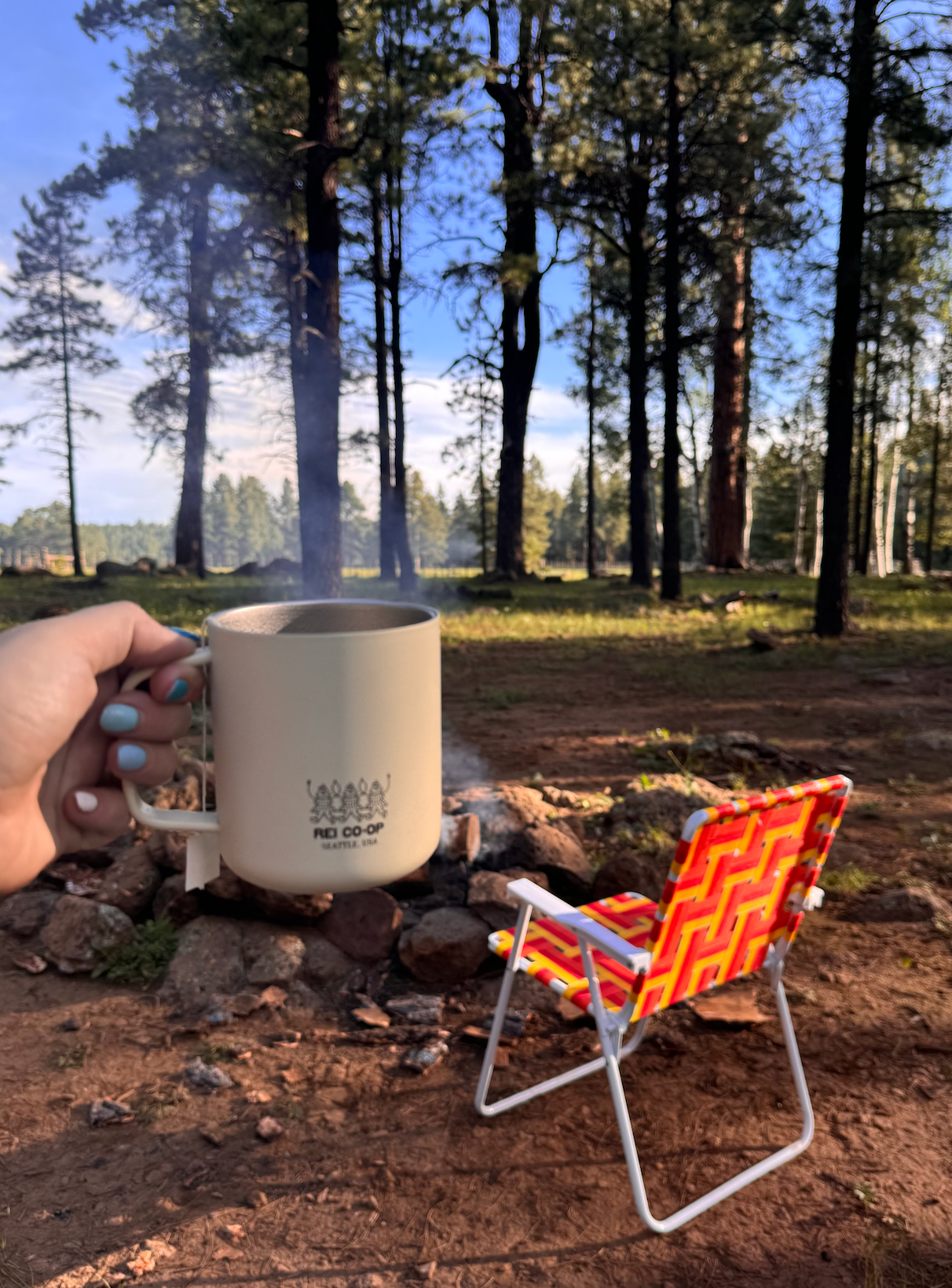 girl holding mug in front of a fire and a camp chair