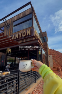 Hand holding an enamel camping mug outside Canyon Coffee, a modern coffee shop near Zion National Park in Springdale, Utah.